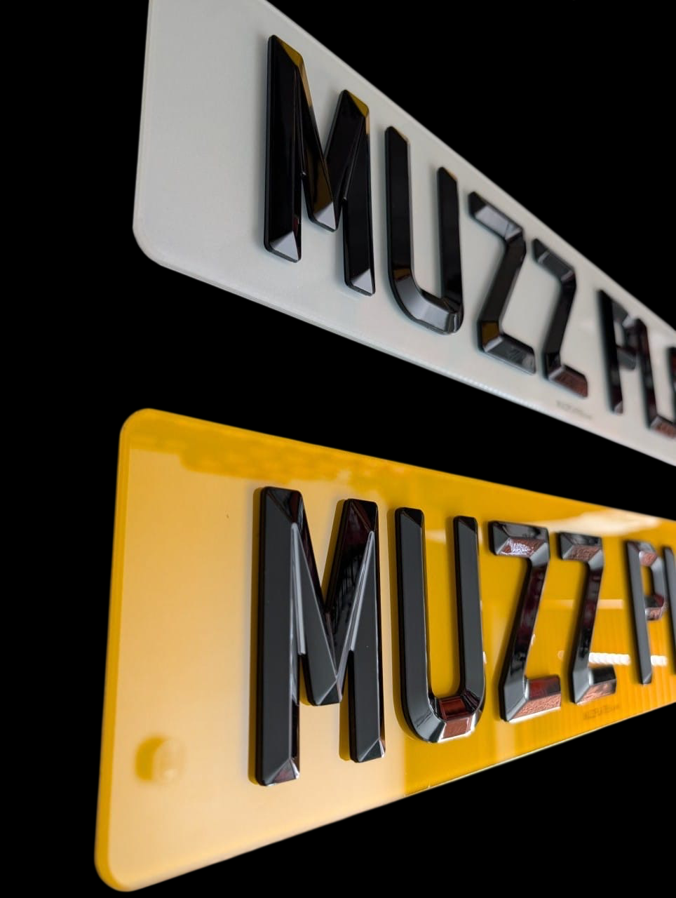 Two bevelled edge number plates one white and one yellow, on a black background.